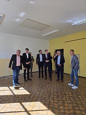Besichtigung der Mittelschule Helmbrechts während des Besuchs des Staatssekretärs Schöffel Neun Männer stehen in einem leeren Klassenzimmer der enträumten Mittelschule Helmbrechts und unterhalten sich.