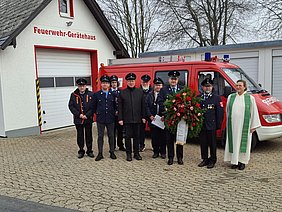 Vertreterinnen und Vertreter der Feuerwehr Ort und Diakonin Twisselmann vor dem Feuerwehrhaus in Ort stehend mit einem Blumengesteck für das Gedenken.
