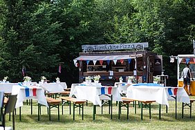 Die in französischen Farben dekorierten Biertischgarnituren stehen auf der Wiese, dahinter sind zwei Verkaufsstände, unter anderem mit Flammkuchen, zu sehen.