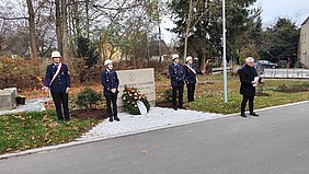 Vier Reservisten und Helmbrechtser Bürgermeister stehen am Gedenkstein in Kleinschwarzenbach zum Volkstrauertag. Ein Blumenkranz ist niedergelegt.