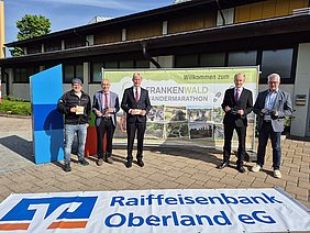 Raiffeisenbank Oberland als Unterstützer zum Frankenwald Wandermarathon Bei Sonne und blauem Himmel stehen zwei Vorstandsmitglieder der Raiffeisenbank Oberland, Bürgermeister des Marktes Marktleugast und Bürgermeister der Stadt Helmbrechts vor der Göbel-Halle als Start- und Zielort.