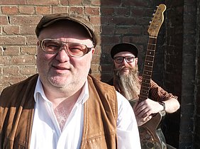 Chris Kramer Duo mit Gitarre vor einer Backsteinhaus