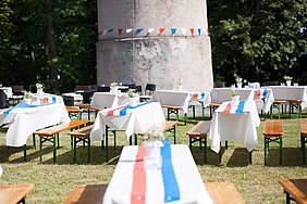 In den Farben der französischen Flagge eingedeckte Biertischgarnituren im Sonnenlicht rund um den Kirchbergturm.