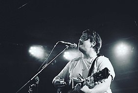 Jim Wilson mit seiner Gitarre am Mikrofon. Schwarz-weißes Bild.