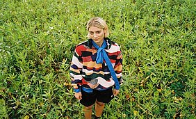 Lener Die Sängerin Lener steht in einem grünen Blumenfeld und sieht direkt in die Kamera
