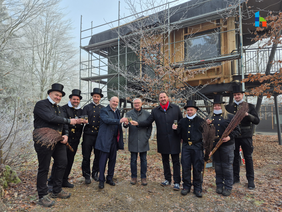 Neun Personen stehen mit Sektgläsern in der Hand vor einem Baumhaus am Kirchberg und stoßen bei winterlichem Sonnenschein auf das neue Jahr an. Darunter sind erster Bürgermeister der Stadt Münchberg, zweiter Bürgermeister der Stadt Helmbrechts und die Kaminkehrer aus beiden Städten