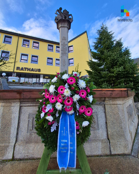Ein mit rosa und weißen Blüten gestalteter Kranz steht am Rathausbrunnen zum Volkstrauertag.