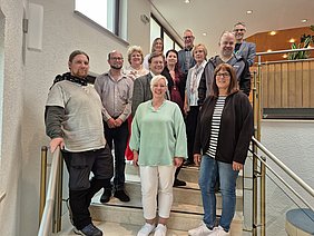 12 Personen, unter anderem sieben Vertreterinnen und Vertreter der begünstigten Einrichtungen, stehen versetzt auf einer Treppe und lächeln in die Kamera