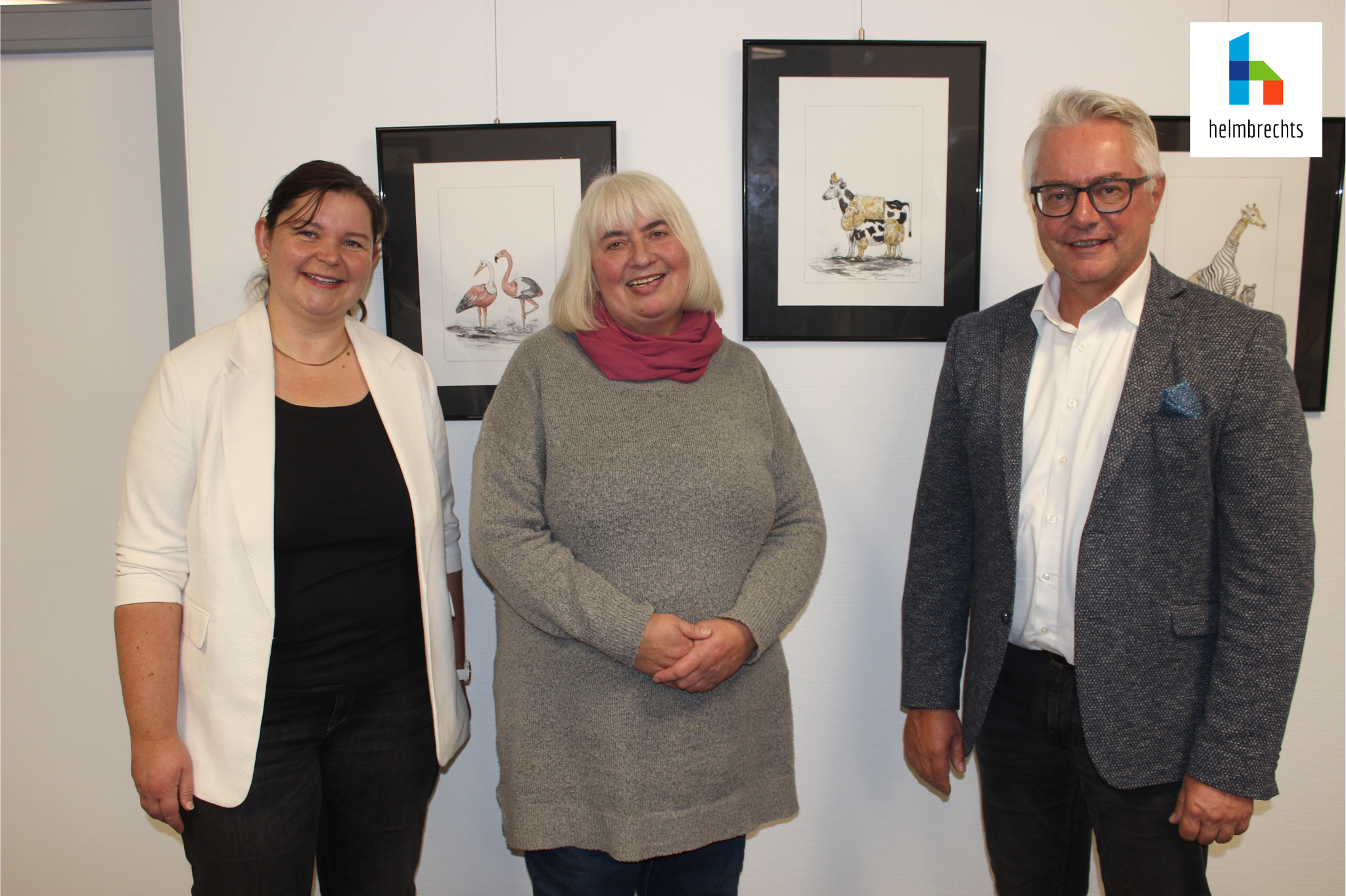 Drei Personen, darunter Bürgermeister und Kulturreferentin der Stadt Helmbrechts sowie Künstlerin Christine Krauß im Rathaus vor ihren gezeichneten Karikaturen zur Ausstellungseröffnung.