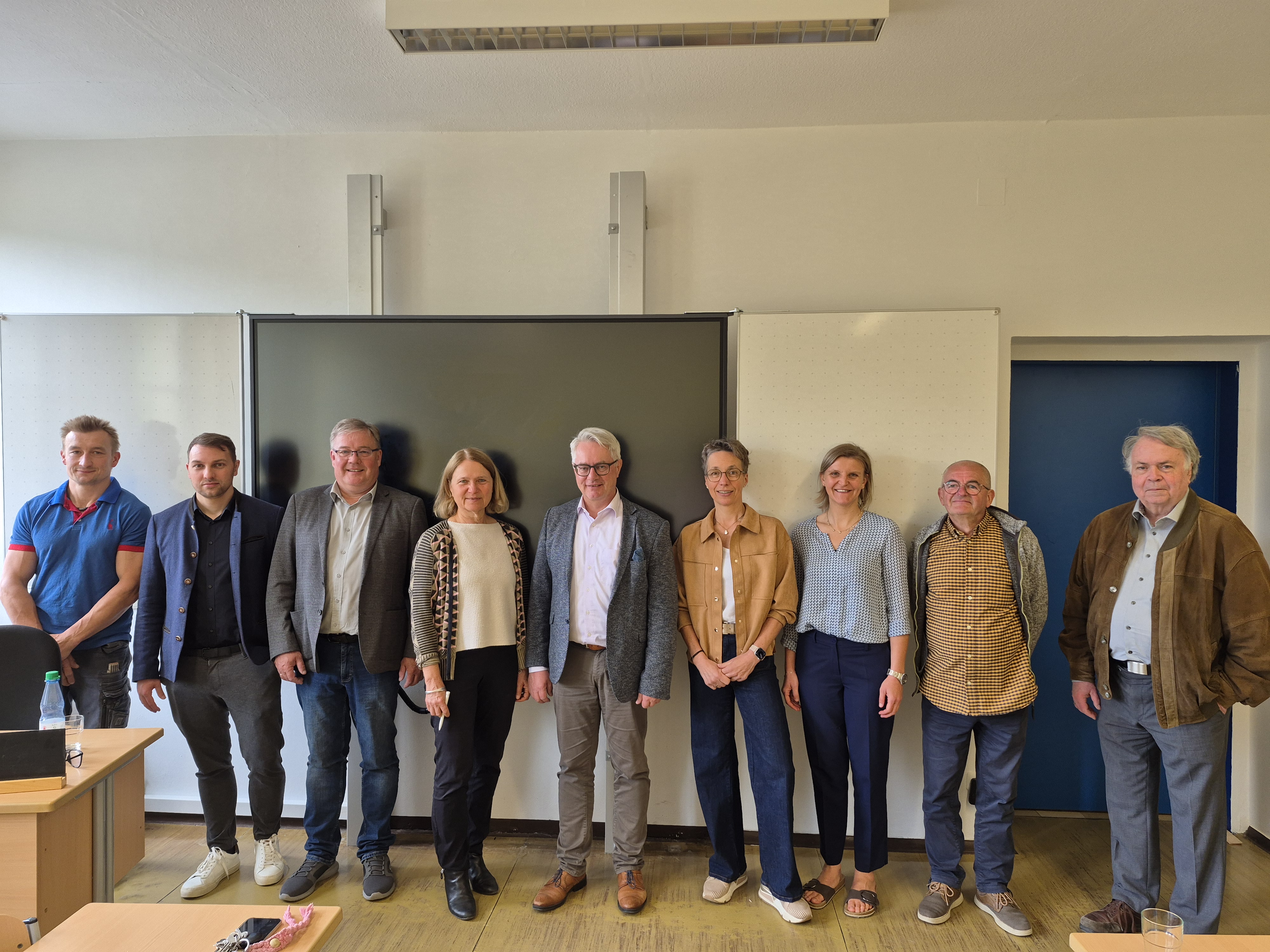 9 Personen des Treffens, darunter Bürgermeister Pöhlmann und Landtagsabgeordnete Ursula Sowa stehen als Gruppe vor der Tafel im Klassenzimmer.
