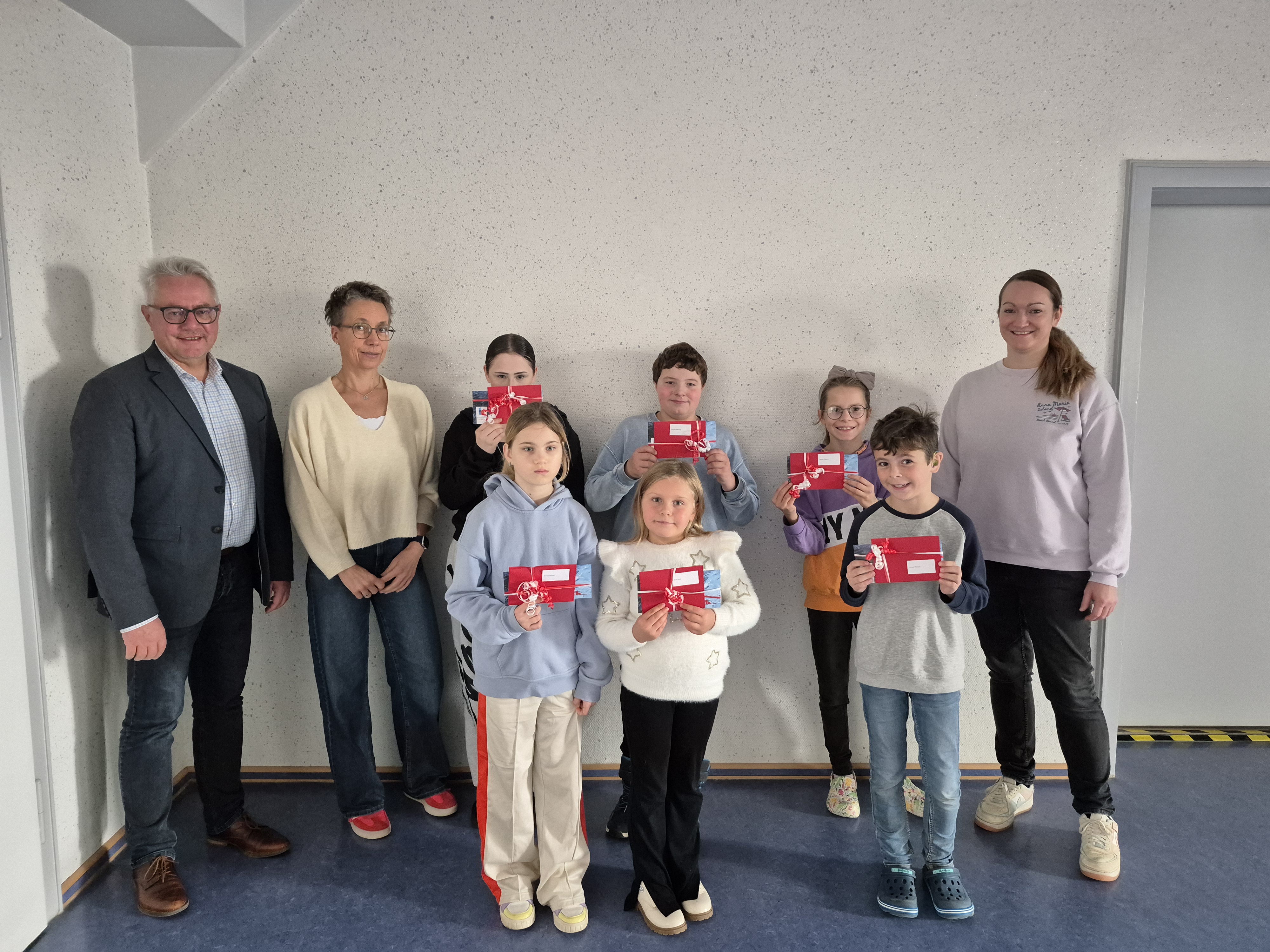 Sechs Kinder stehen in der Mitte zwischen zwei ihrer Lehrinnen und dem Helmbrechtser Bürgermeister. In der Aula, vor einer weißen Wand. Sie halten ihre Gewinne in die Luft.
