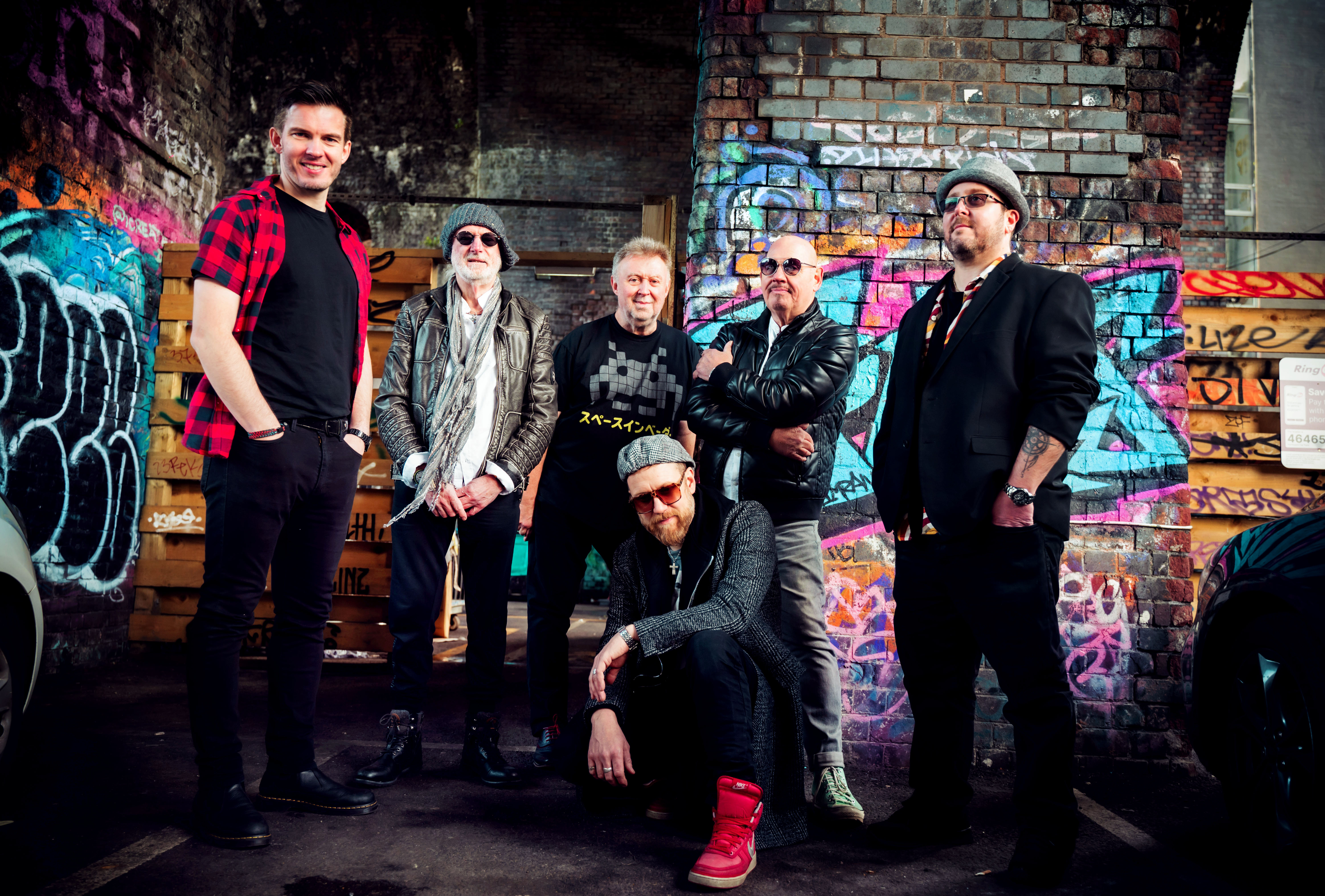 Die sechsköpfige Climax Blues Band auf einem Gruppenfoto unter einer Unterführung, deren gemauerten Wände mit Graffiti besprüht sind.