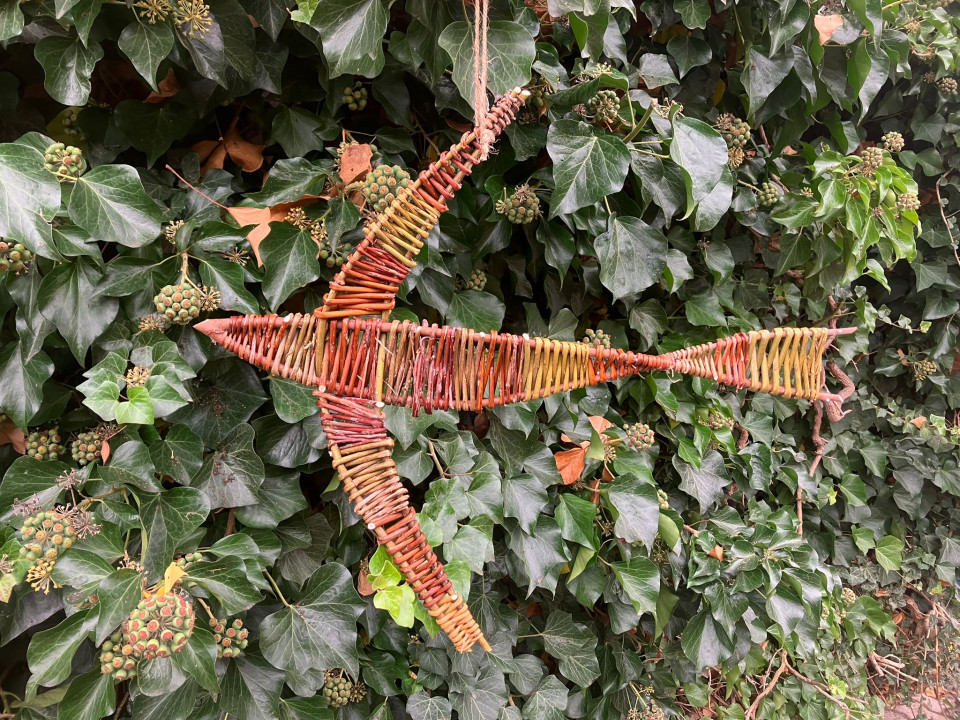 Ein aus Weidenästen geflochtener Vogel vor einer grünen Hecke
